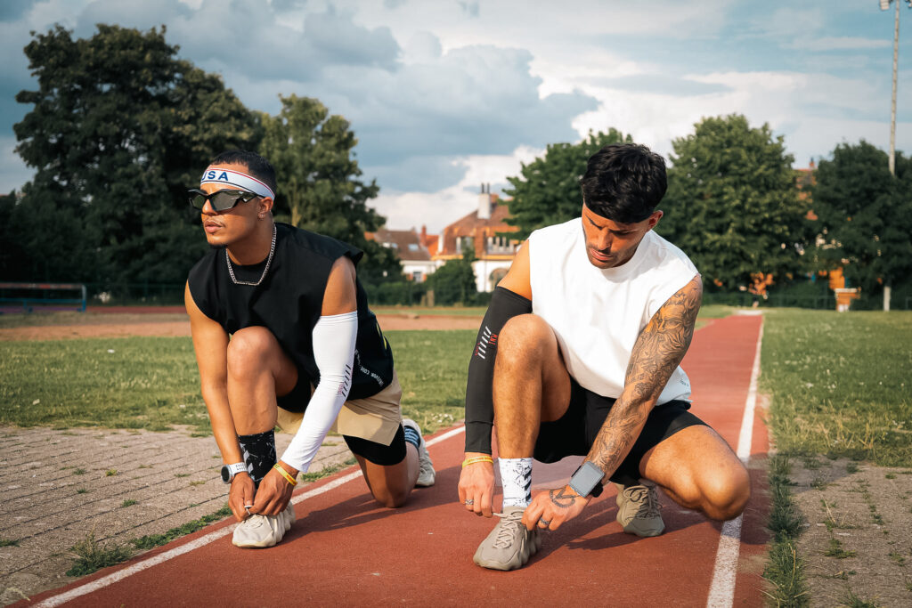 Two young men tying their shoelaces on a running track.